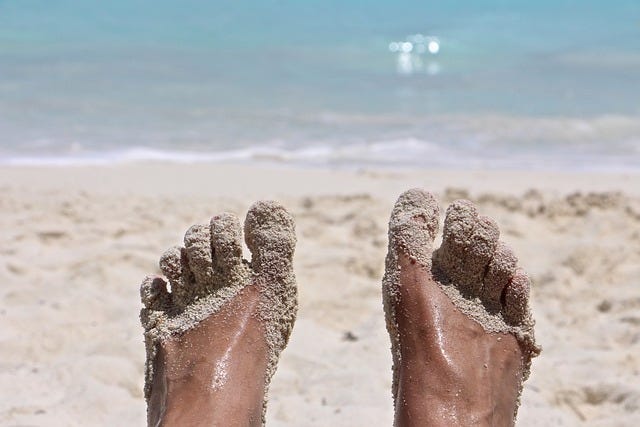 A pair of sand-covered feet on a lovely white sand beach with the ocean in the background A pair of sand-covered feet on a lovely white sand beach with the ocean in the background