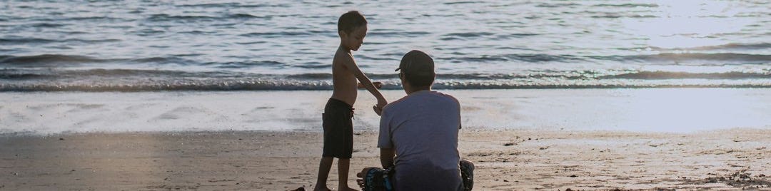 2 men sitting on beach shore during daytime