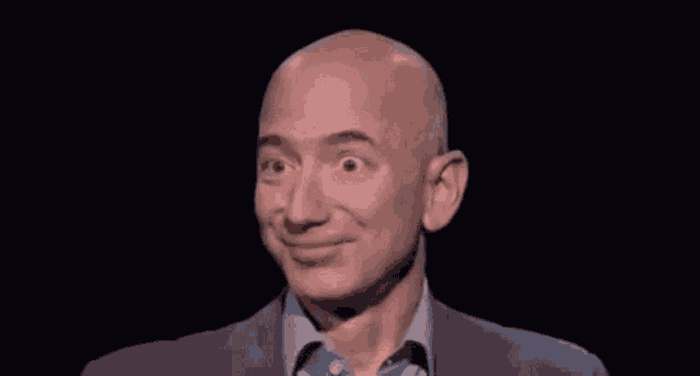 a bald man in a suit and blue shirt is smiling against a black background .