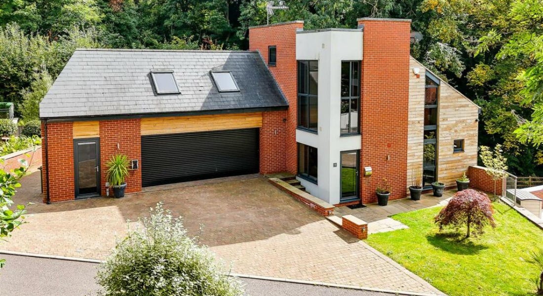 A brick house with a black roof and white walls surrounded by greenery