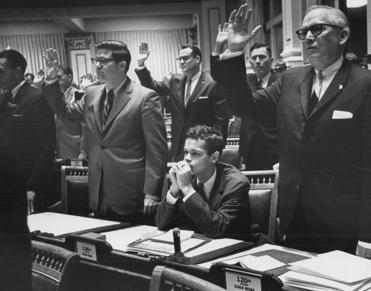 B&W photo of Julian Bond seated while white legislators are sworn in. B&W photo of Julian Bond seated while white legislators are sworn in.