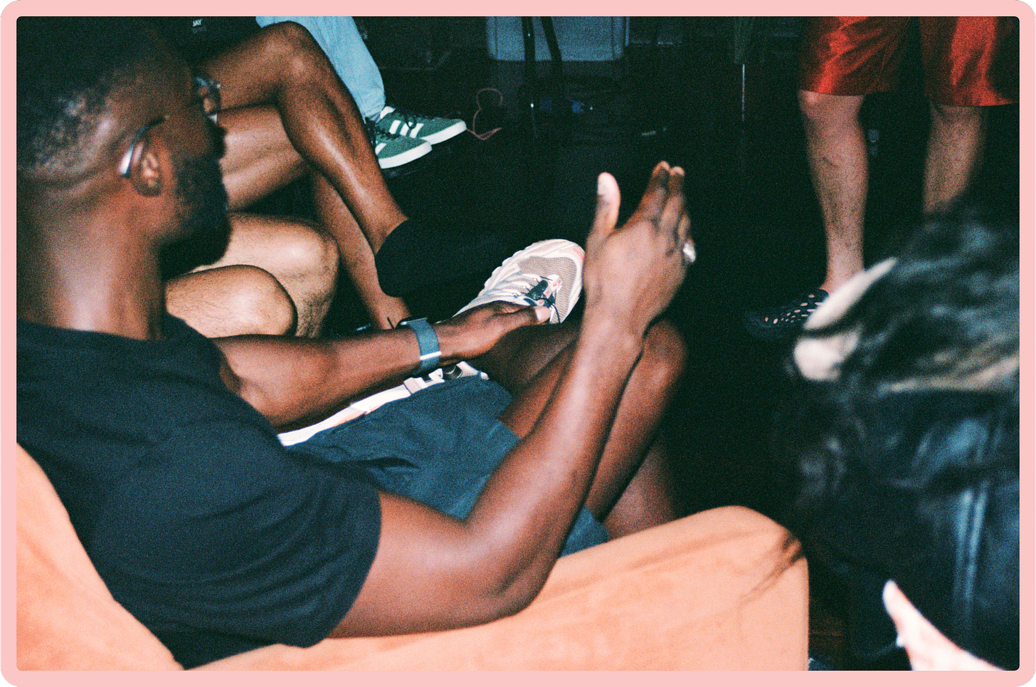 A photo, in side profile, of a young Black man sat on an orange sofa. His hands are animated, moving as if he is talking.