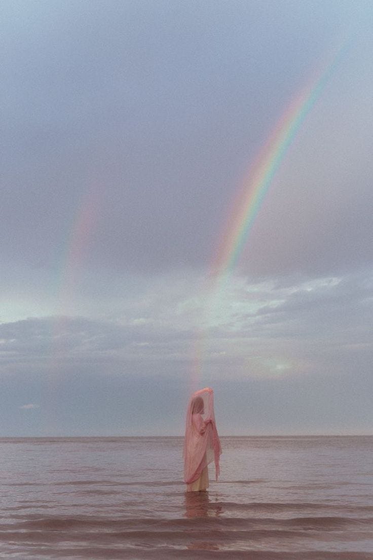 This may contain: a woman standing in the ocean under a rainbow