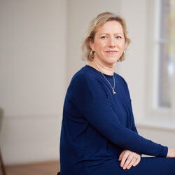 A blond woman looks at the camera in a navy blue top