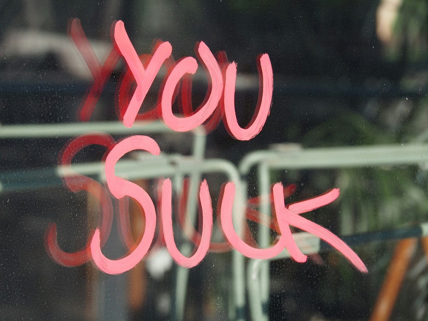 Image of the words You Suck written with pink lipstick on a window