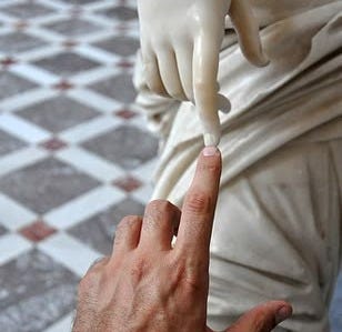 This may contain: a hand reaching for something in front of a white statue with one hand on it's finger