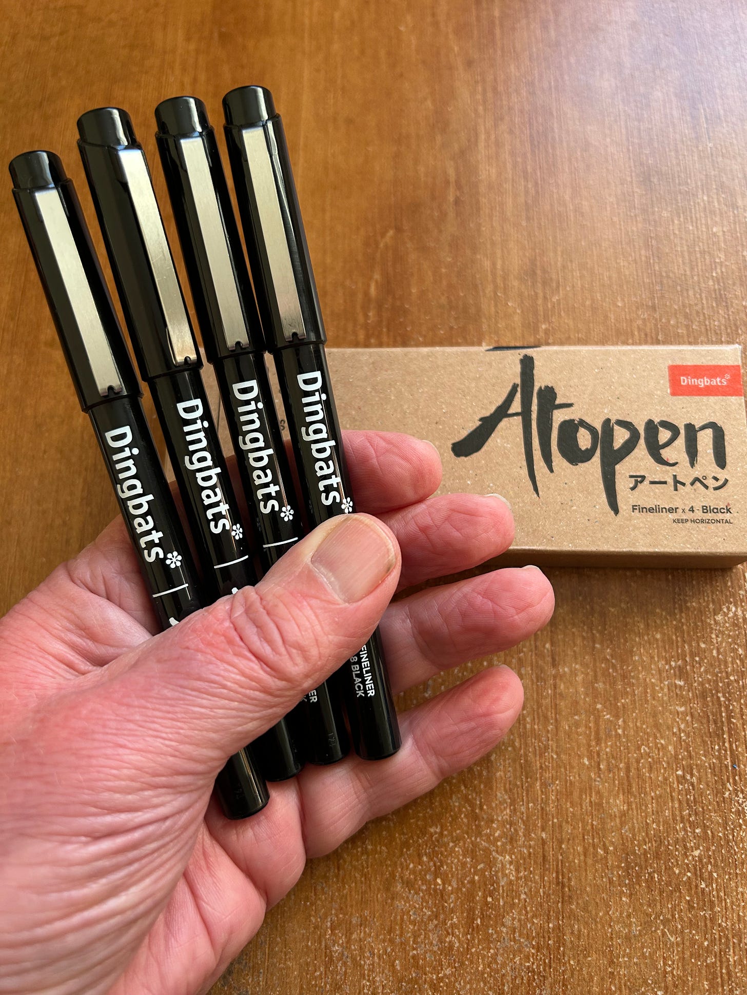 Four Atopen Fineliner pens from Dingbats. Held in the hand of the author, Roland Millward. The pens are black. Below them is the original box in which they arrived with Atopen written on it. Four Atopen Fineliner pens from Dingbats. Held in the hand of the author, Roland Millward. The pens are black. Below them is the original box in which they arrived with Atopen written on it.