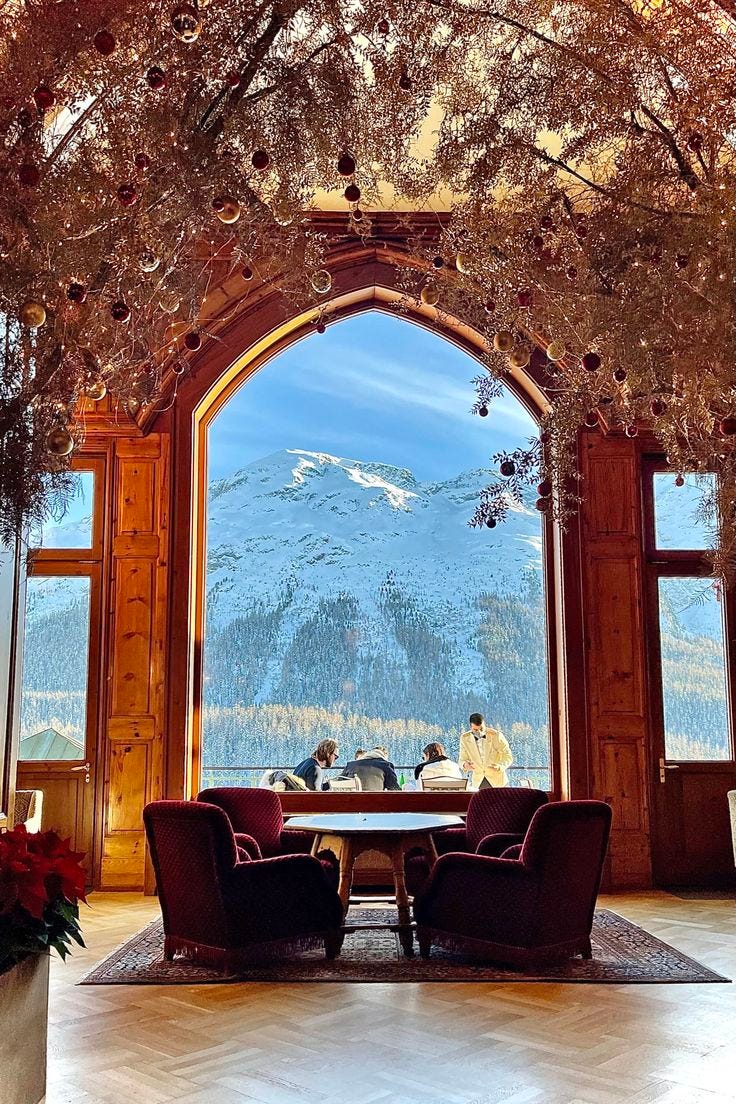 This may contain: two people sitting at a table in front of an open window with mountains behind them This may contain: two people sitting at a table in front of an open window with mountains behind them