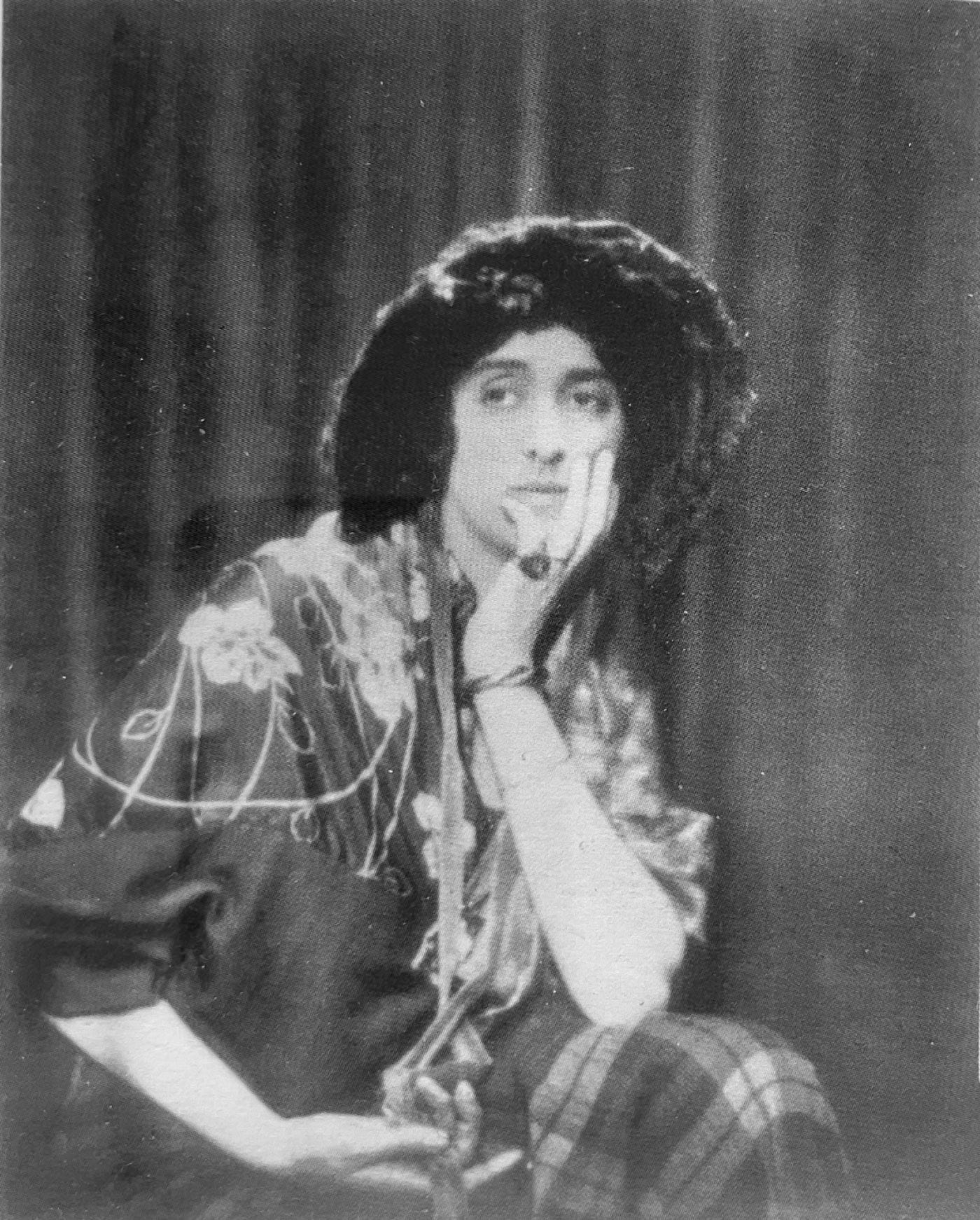 A woman wearing a bonnet sits with her head in a hand and elbow resting on her knee.