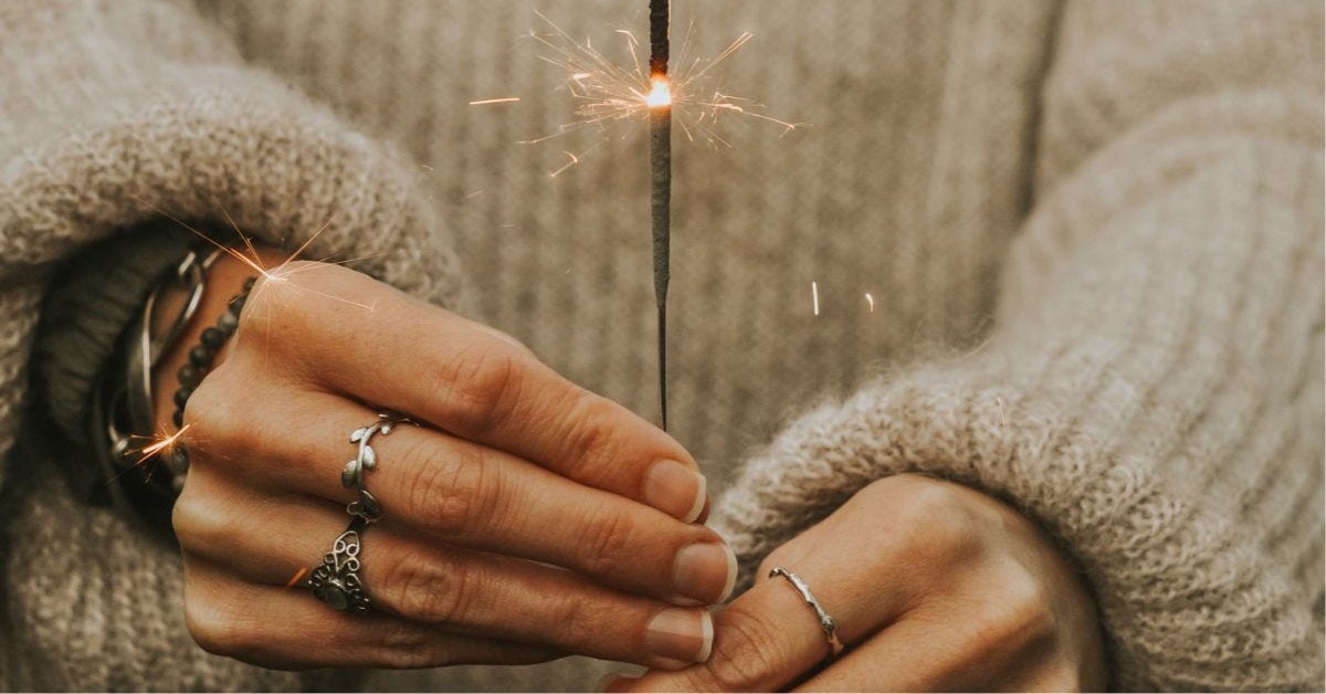 A photography to represent the Self-belief Coaching - it shows a close up of hands holding a lit sparkler. The person is wearing bracelets, rings and a cream knitted jumper