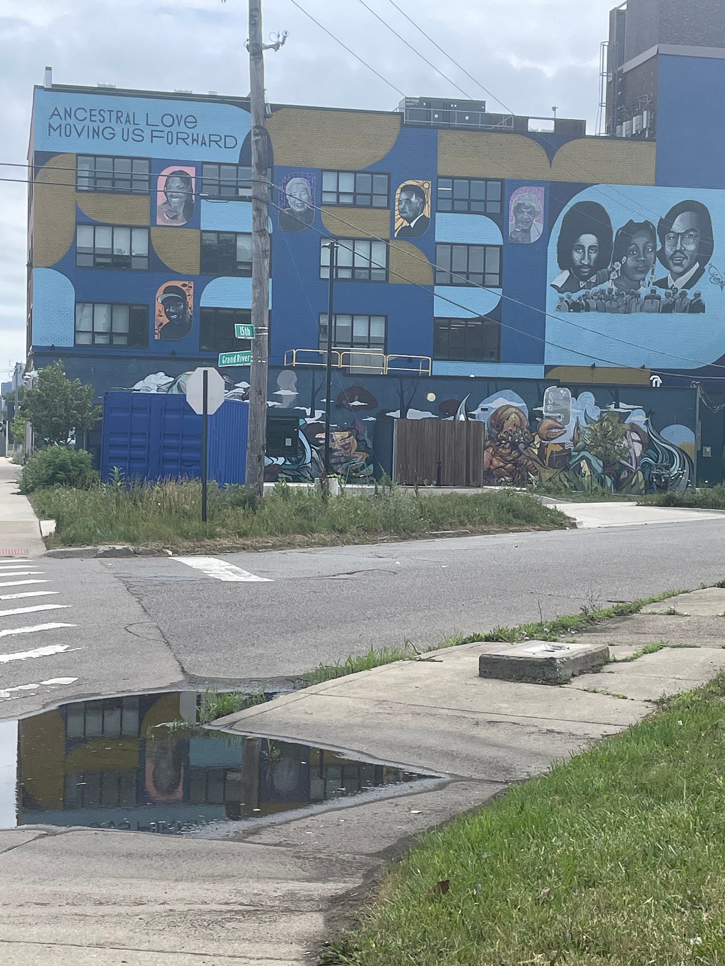image of the love building exterior in detroit, a four story building with a mural in blue tones that reads ANCESTRAL LOVE MOVING US FORWARD with images of many ancestors, mostly Black and Asian, including Charity Hicks and Grace Lee Boggs image of the love building exterior in detroit, a four story building with a mural in blue tones that reads ANCESTRAL LOVE MOVING US FORWARD with images of many ancestors, mostly Black and Asian, including Charity Hicks and Grace Lee Boggs