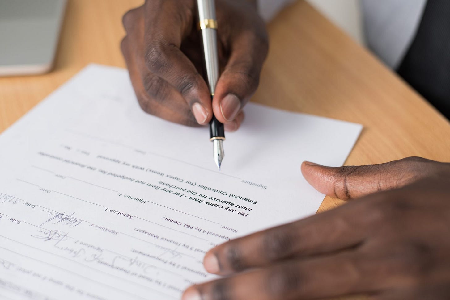 Photo by Cytonn Photography on Pexels Close-up of a man's hands signing a formal document indoors. (stock photo)