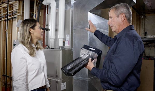 An HVAC technician showing a homeowner an APCO-X unit, representing customer trust and professional service. An HVAC technician showing a homeowner an APCO-X unit, representing customer trust and professional service.