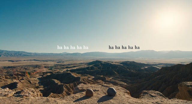 Imagem de uma cena de Tudo em Todo Lugar ao Mesmo Tempo. Em uma paisagem deserta, duas pedras redondas aparecem em primeiro plano. Por cima da imagem há o texto "ha ha ha ha ha"