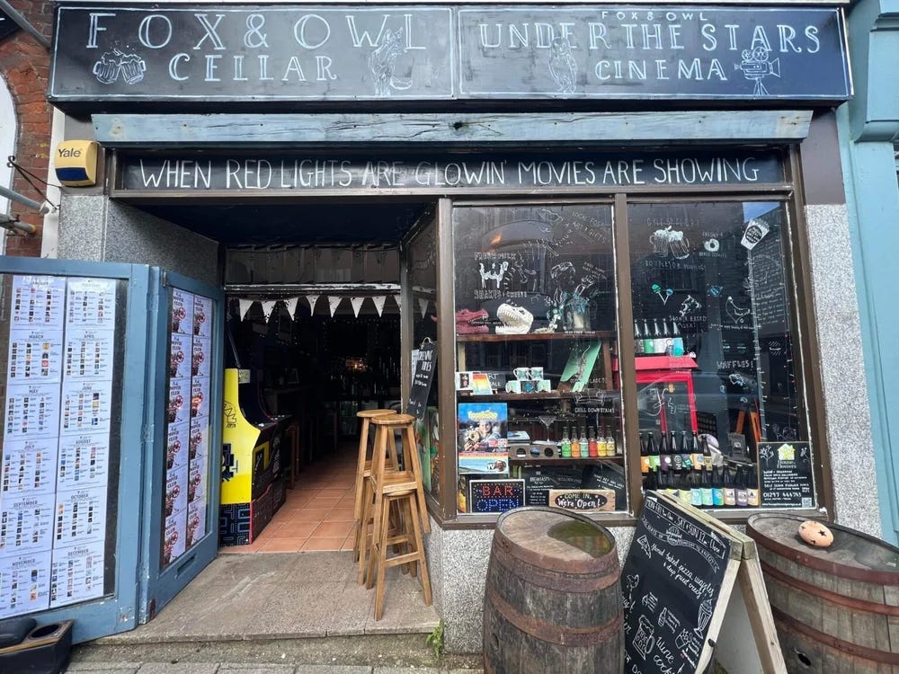 Outside of the bar, with handwritten sign "when red lights are glowin' movies are showin" referring to the downstairs cinema "Under the Stars"