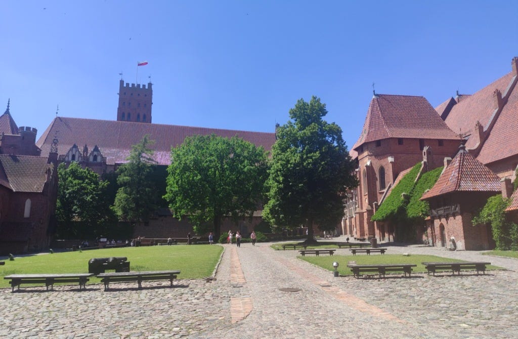 Brick buildings and a tall tower surround a cobbled courtyard with green lawns at the lower castle