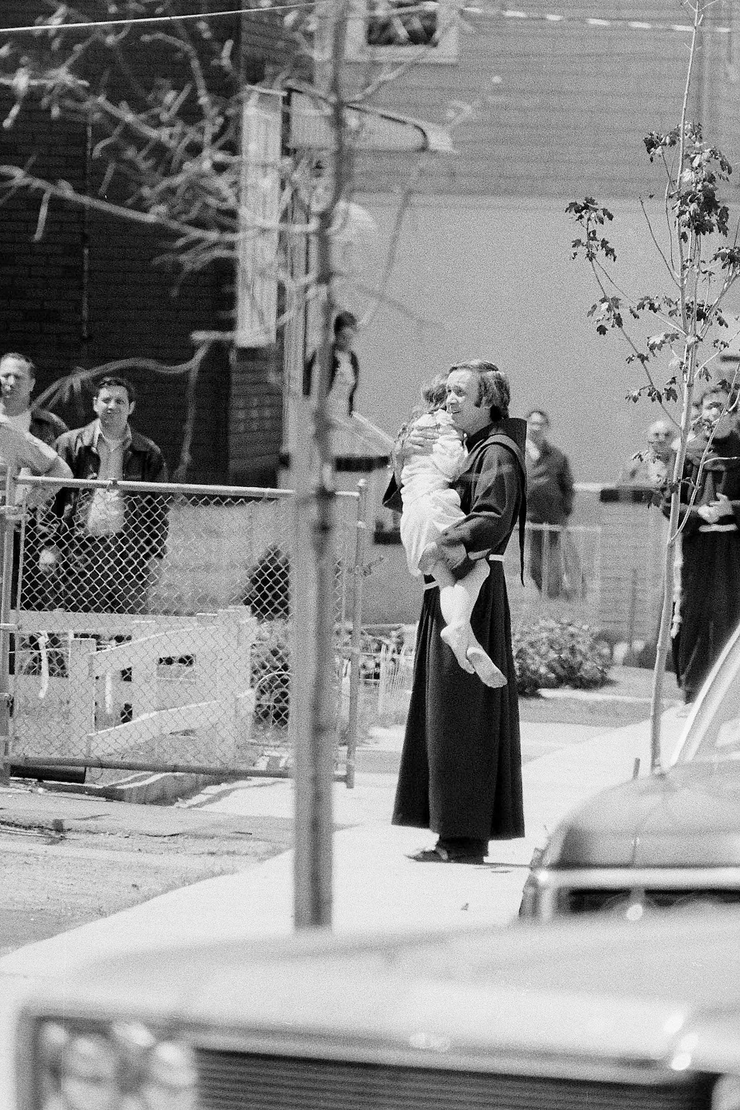 Father Mychal Judge in his Franciscan habit carries a child on a city street