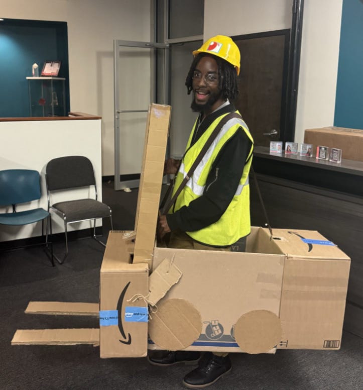 Me wearing a yellow hardhat, a high-vis safety vest, and a cardboard forklift costume I made myself and wore via suspenders.