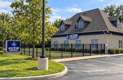 Ascend Dispensary brick building exterior with logo sign, black fence, and landscaping