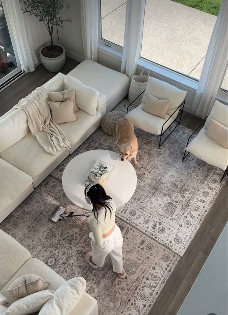 This may contain: a woman standing in front of a living room window next to a couch and coffee table