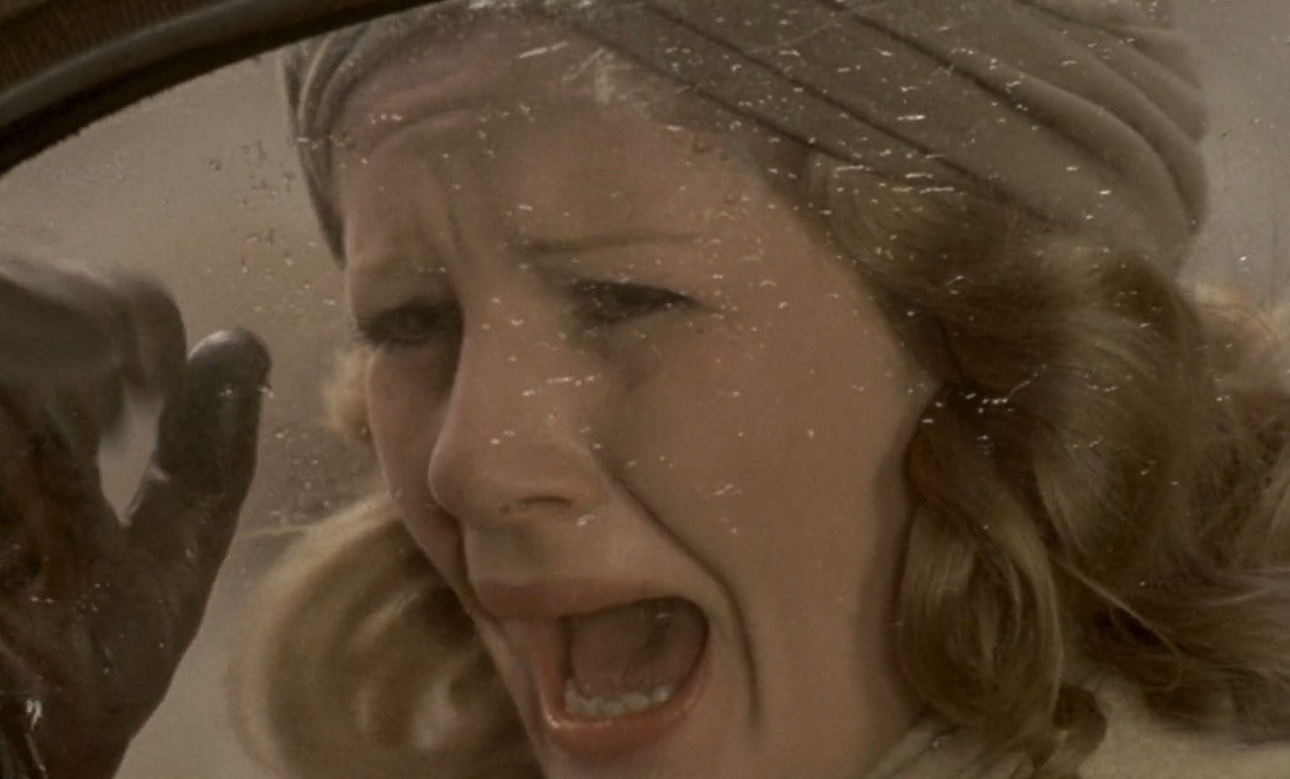 Dominique Sanda, wearing a turban, pounds on a car window, her mouth twisted in a scream.