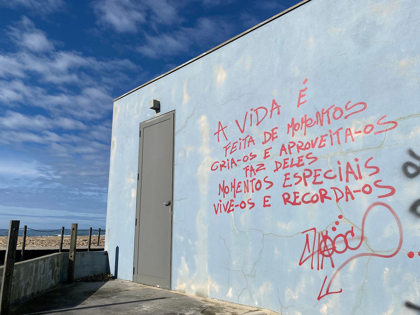 Graffiti in Portuguese on a building wall by a beach: 