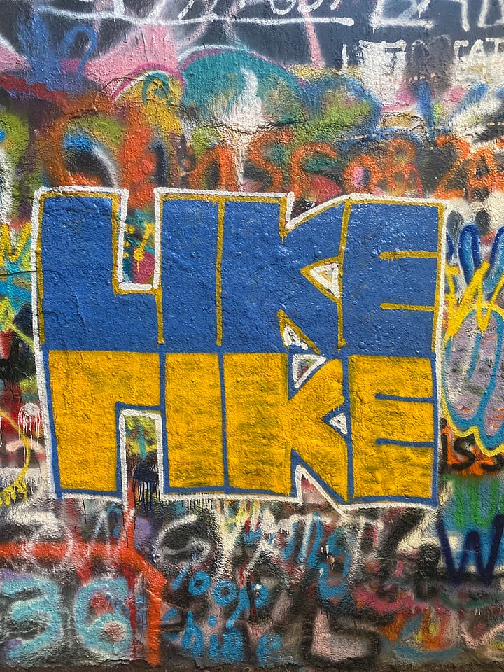 Black, white, and pink "DOWN" on a graffiti wall, over 100 handwritten "aesthetic" stickers on a rolling chair, "Like" painted in blue, yellow, and white facing up and down, and "motherquake" painted in black on a yellow square.