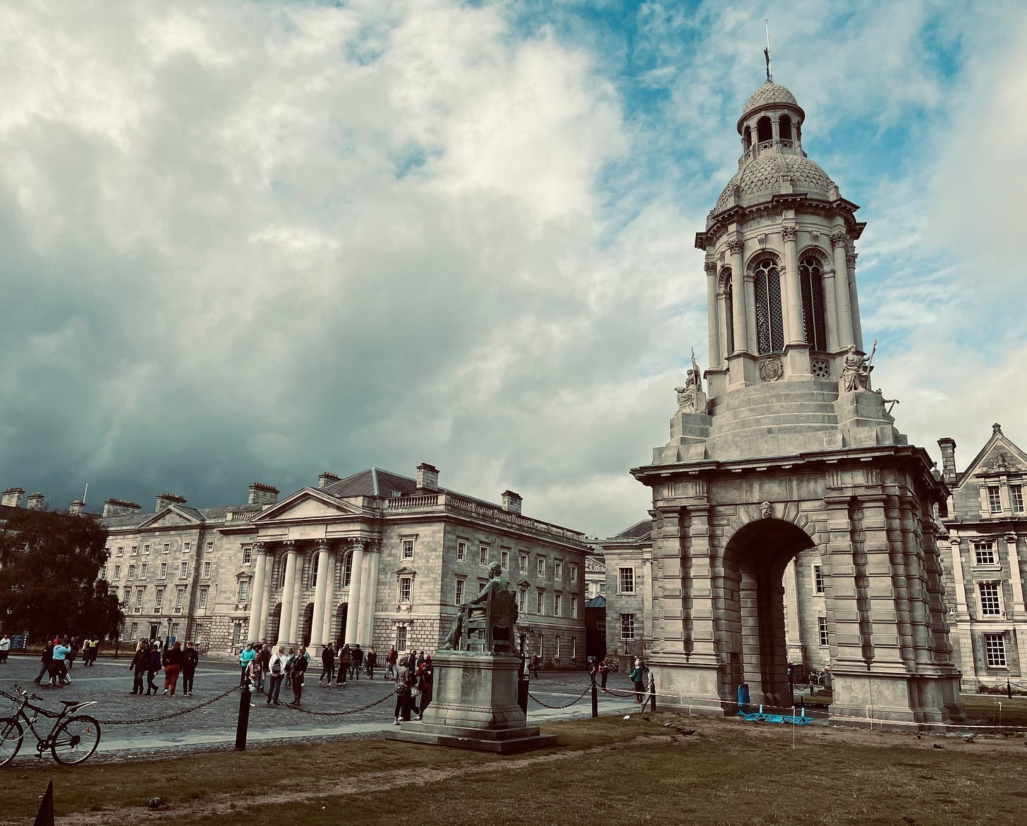 A building with a tower and people walking around

Description automatically generated