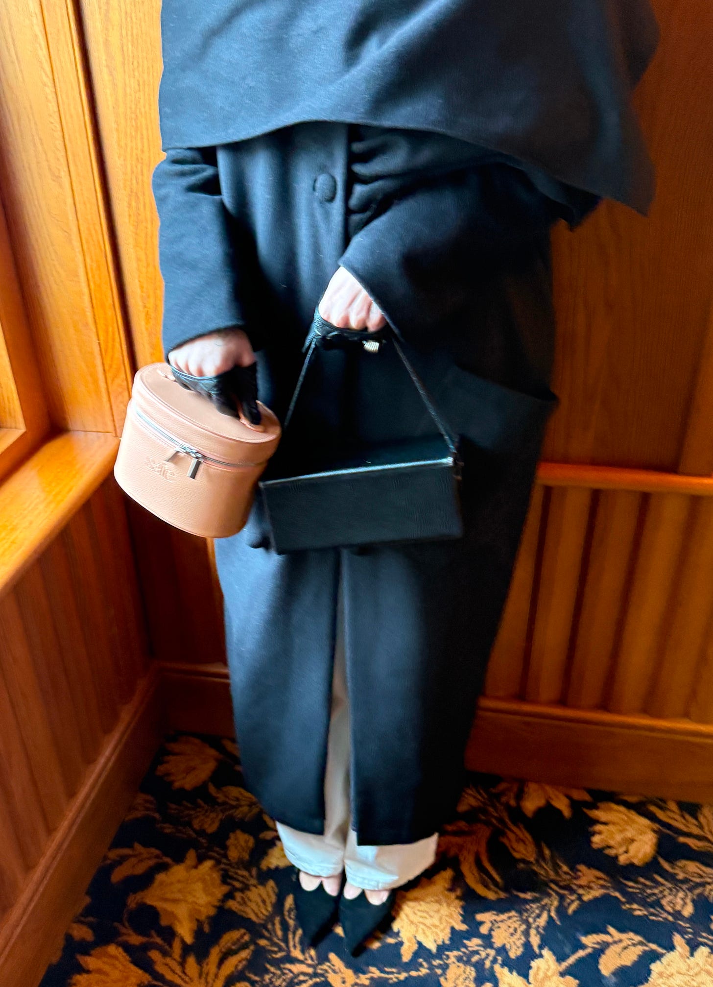 A woman holding a pink Saie vanity case and a black handbag.