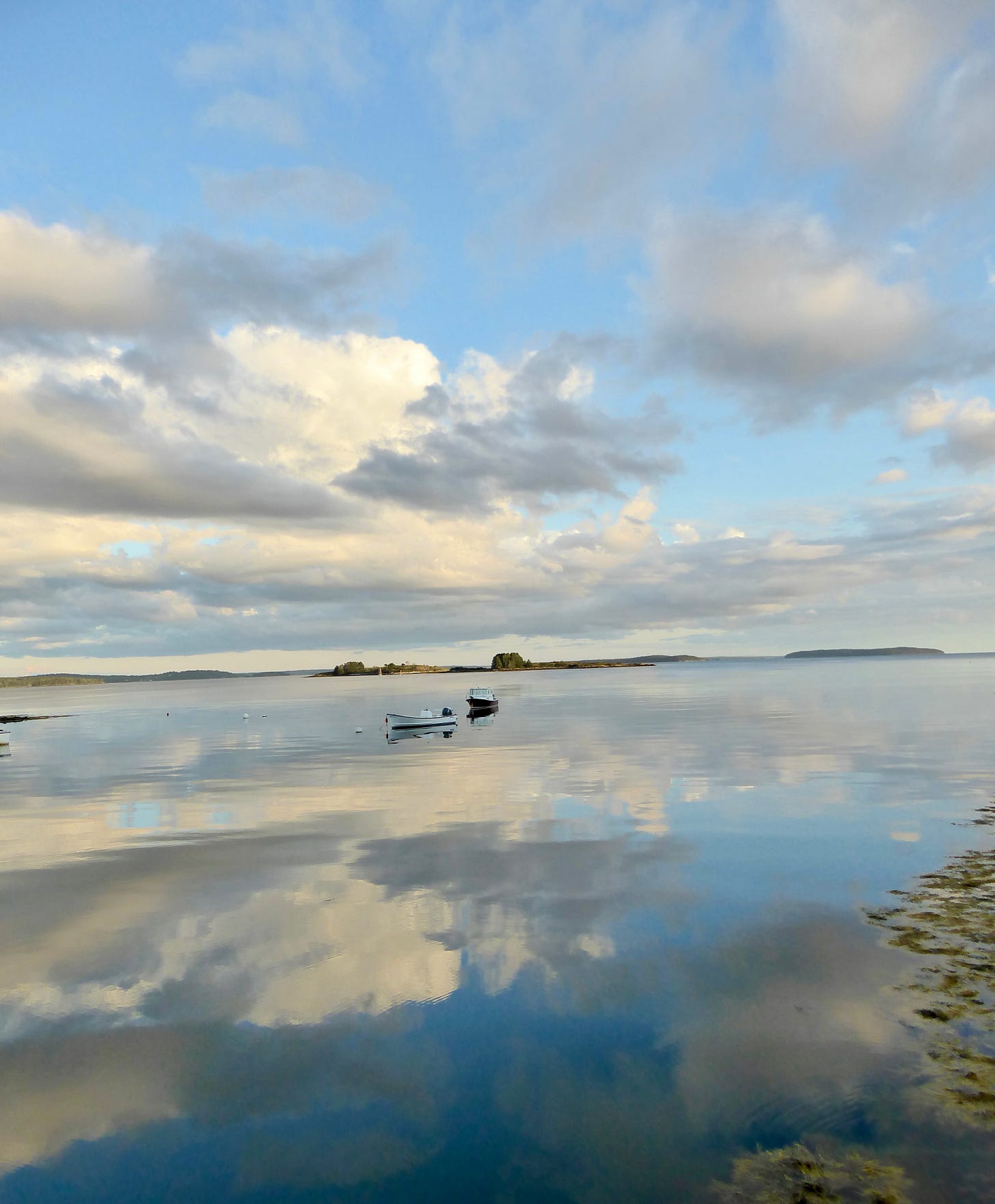 A Seaview with puppy clouds against a gorgeous blue sky. The clouds are reflected in the still water