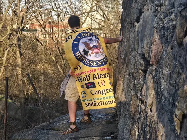 Man wrapped in a large yellow congressional banner standing on a ledge near a stone wall, partially turned away from the camera. Man wrapped in a large yellow congressional banner standing on a ledge near a stone wall, partially turned away from the camera.
