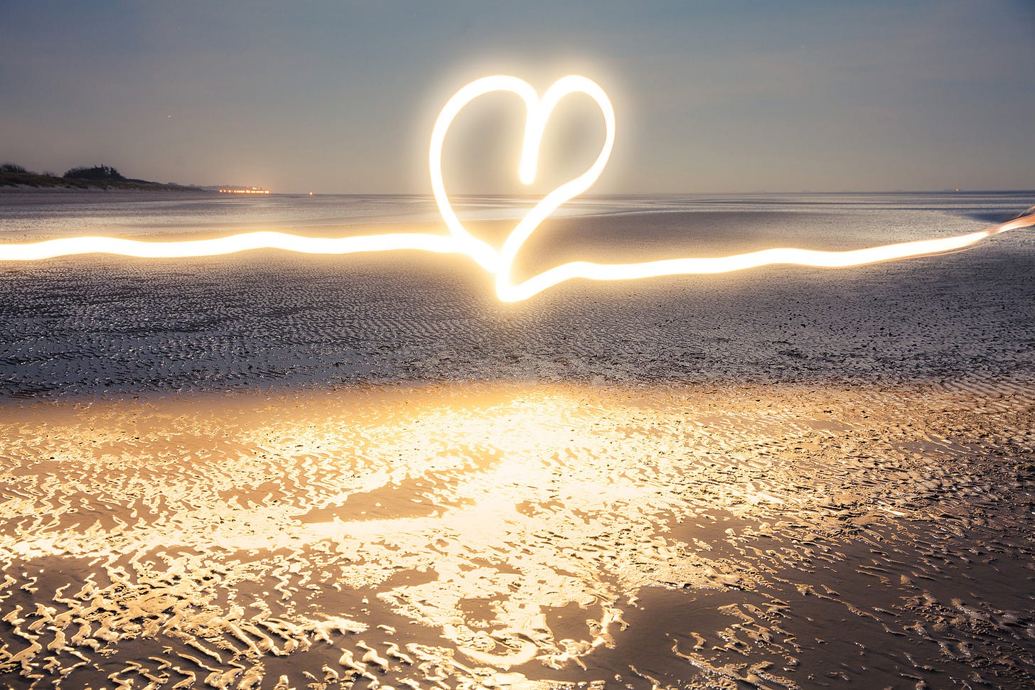 A glowing heart drawn with flashlight at blue hour on the beach near the water at low tide A glowing heart drawn with flashlight at blue hour on the beach near the water at low tide
