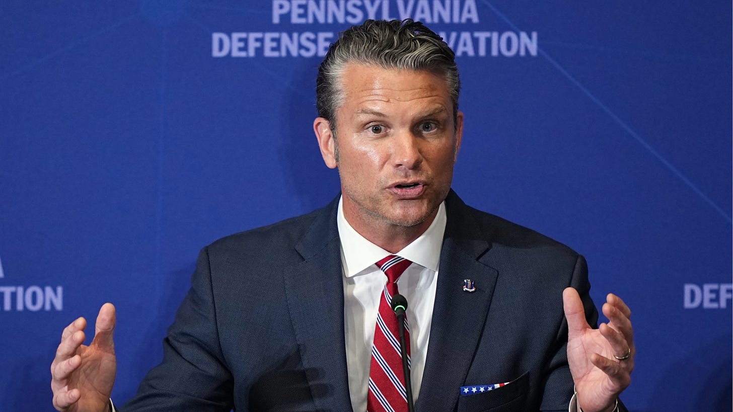 Secretary of War Pete Hegseth gesturing as he speaks at a podium before a blue backdrop Secretary of War Pete Hegseth gesturing as he speaks at a podium before a blue backdrop
