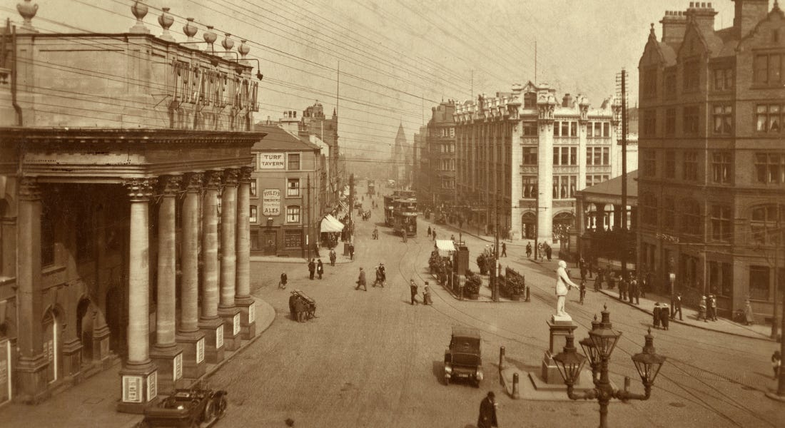 A view of the Theatre Square in Nottingham with a theatre to the left, buildings on all corners, and cars driving down the road A view of the Theatre Square in Nottingham with a theatre to the left, buildings on all corners, and cars driving down the road