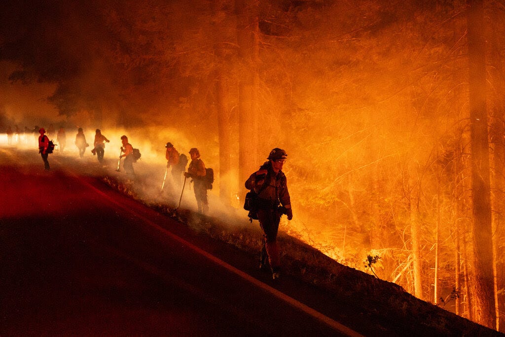 Firefighters walk along a ridge lit by orange light from nearby fires.