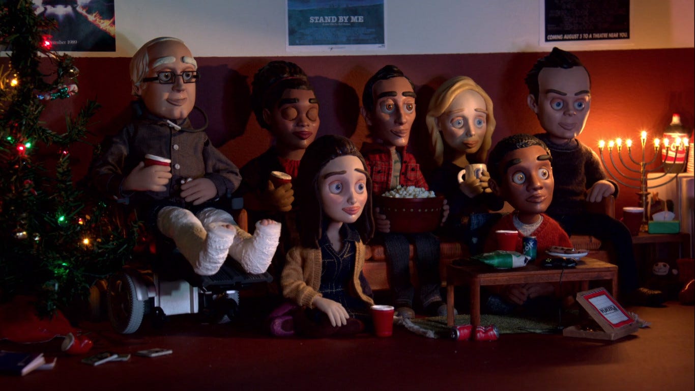 Claymation versions of the Community cast, sat on a sofa between a Menorah and a Christmas tree, with a bunch of snacks
