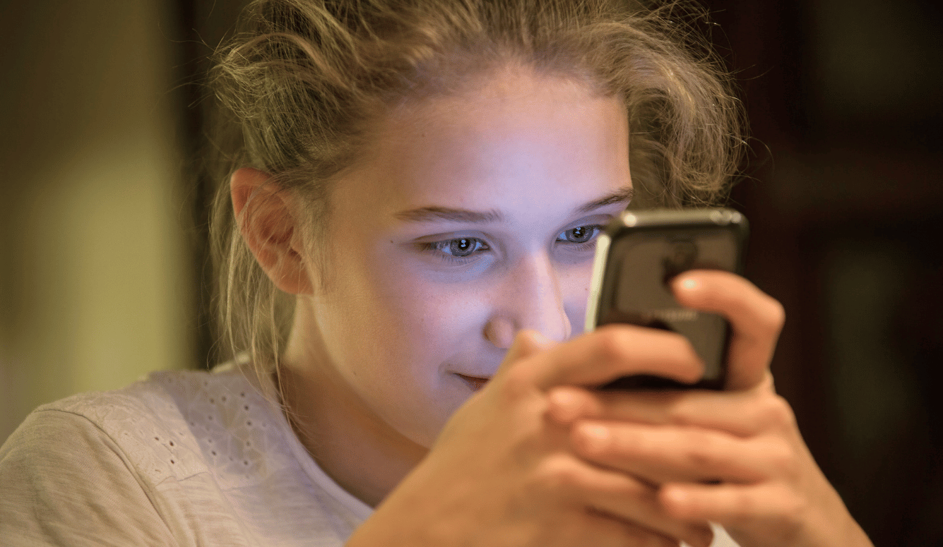 A young woman holds a mobile phone up to her face, her eyes intent on the screen. A young woman holds a mobile phone up to her face, her eyes intent on the screen.