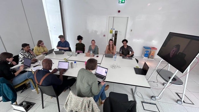 Photo of AI in the Street project members in a meeting, sat at a large table and viewing a display.