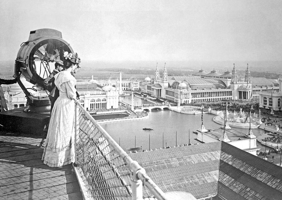 A black-and-white photograph from 1893 showing several people standing along a fence on top of a building, looking out over a large fairground filled with ornate buildings.
