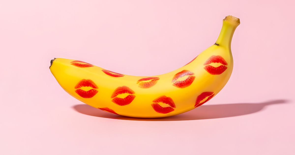 Yellow banana covered in red lipstick kiss marks, photographed against a soft pink background in a playful, pop-art style.