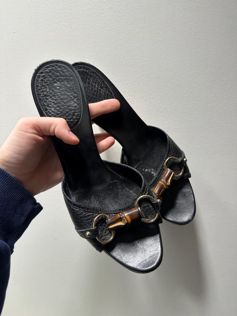 May include: A pair of black leather heeled sandals with gold hardware and brown bamboo accents.