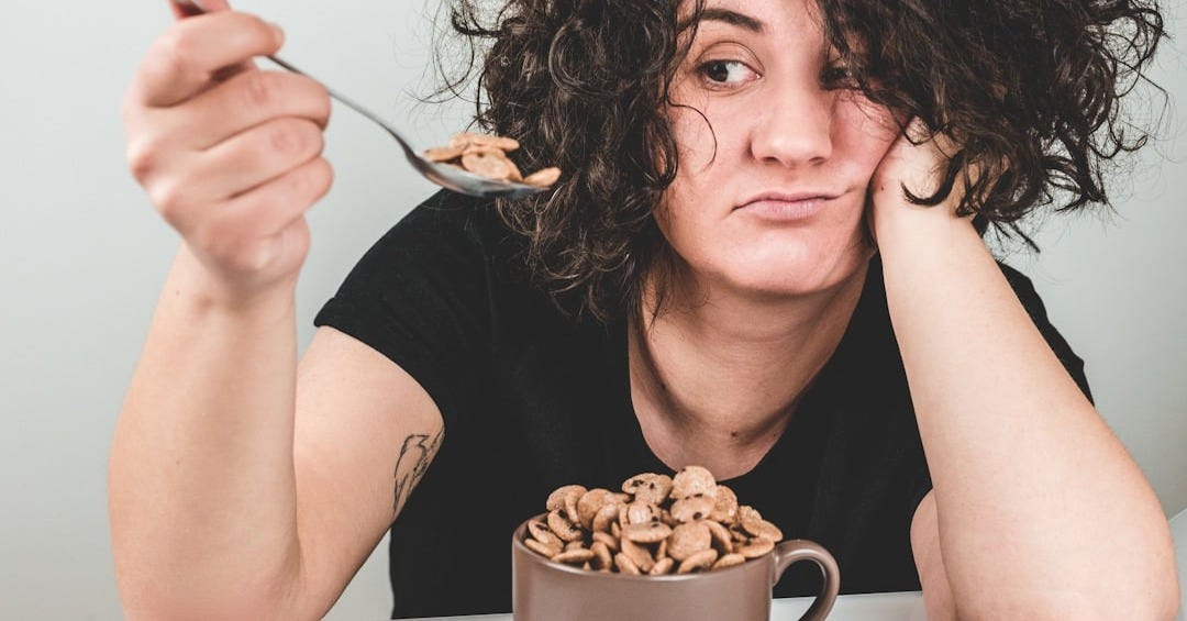 woman with messy hair wearing black crew-neck t-shirt holding spoon with cereals on top woman with messy hair wearing black crew-neck t-shirt holding spoon with cereals on top