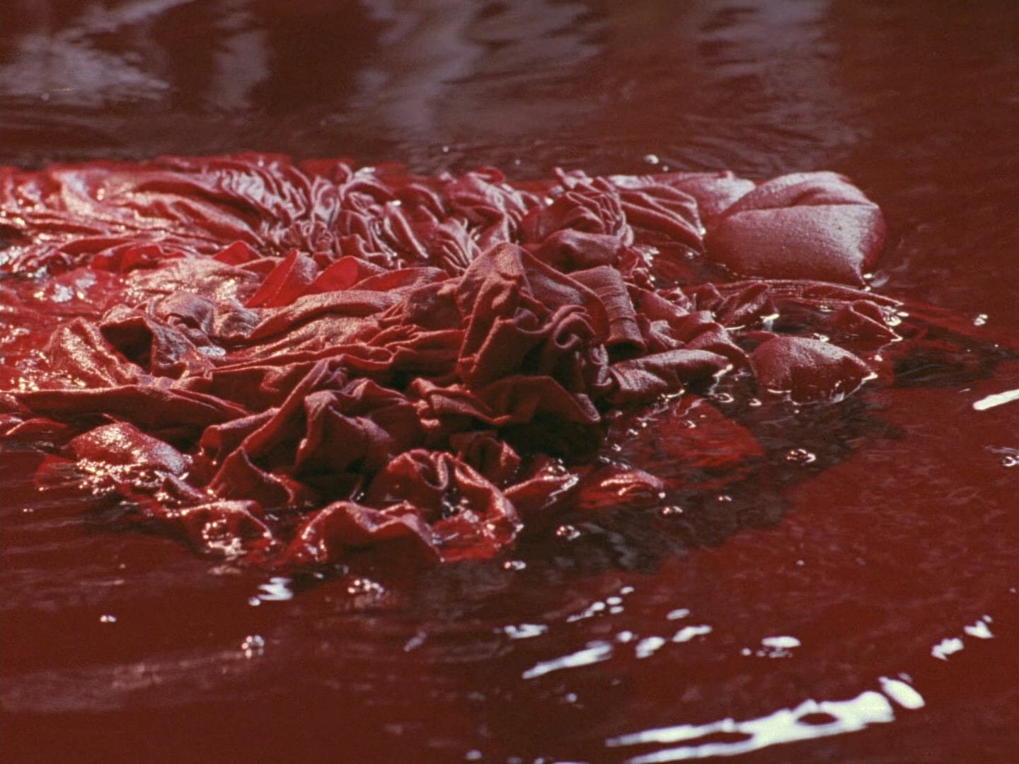 Red textiles float in a vat of dye in "Ju Dou" (1990)