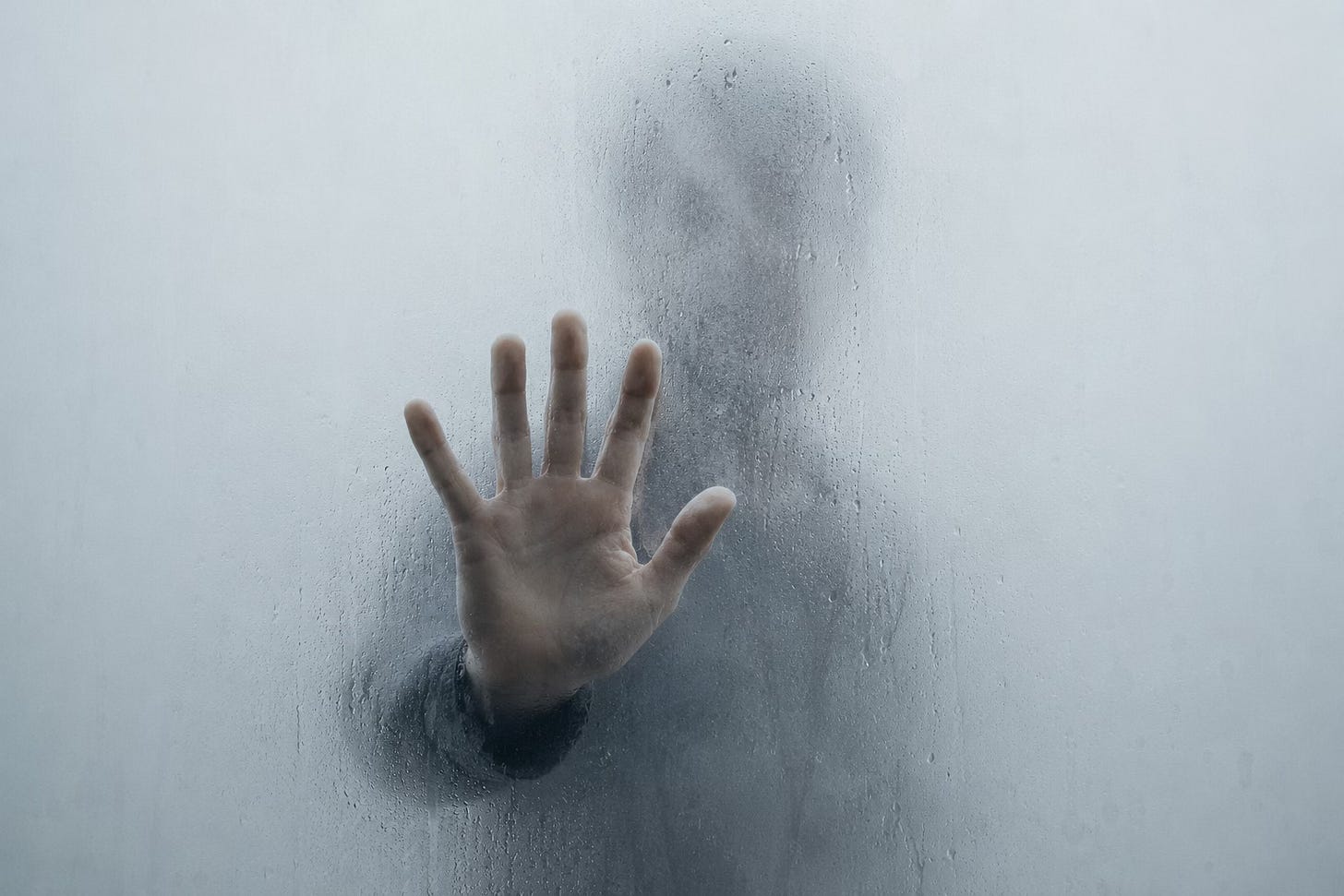 A hand pressed against foggy glass, a faint figure disappearing behind it