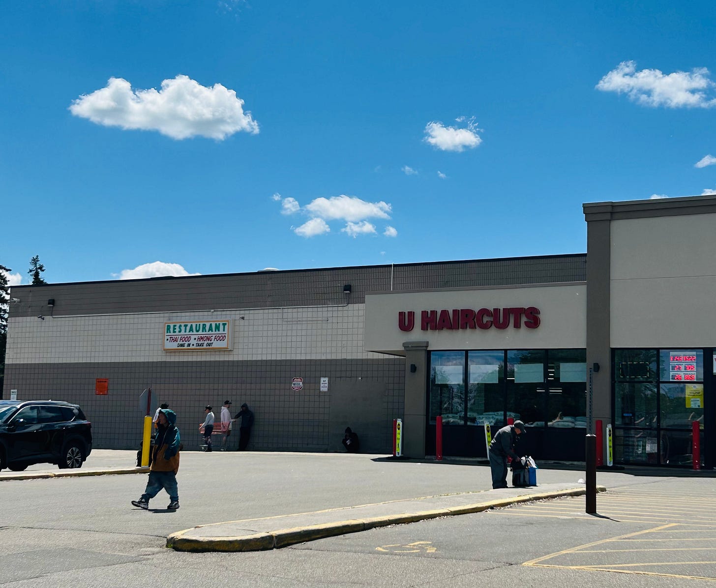 Picture shows a grocery store with various people walking out and two strangers praying in the distance among blue skies and toy story clouds. Picture shows a grocery store with various people walking out and two strangers praying in the distance among blue skies and toy story clouds.