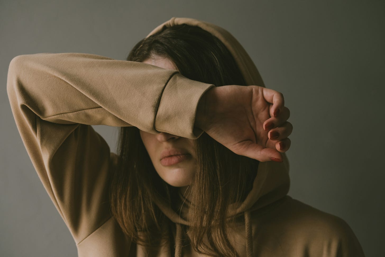 A woman in a brown hoodie covering her eyes with her arm.