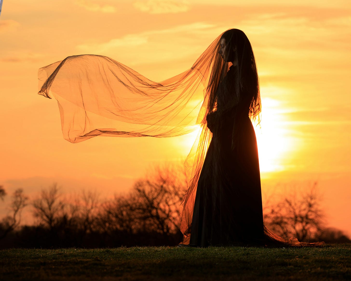 A lone woman clothed in black with veil blowing against a sunset sky A lone woman clothed in black with veil blowing against a sunset sky