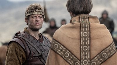 James Norton in character as King Harold talking to another character on a battlefield. James wears a gold crown and armour.