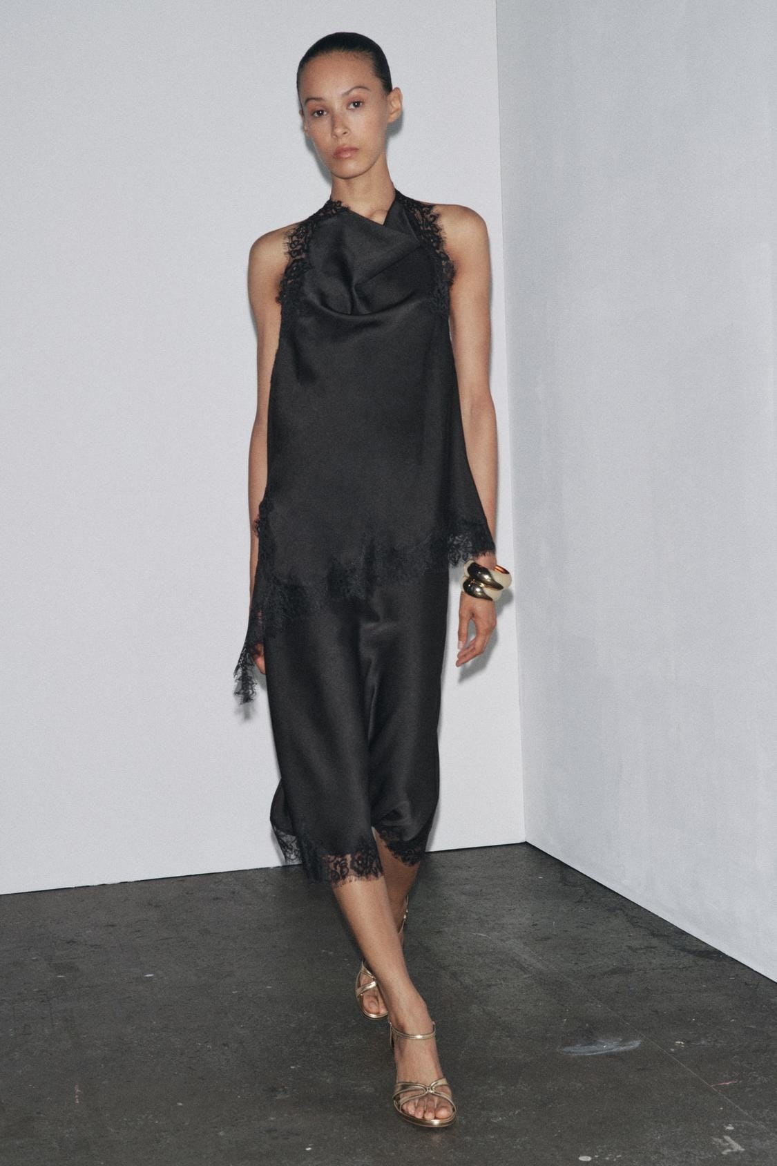 Black halter neck top with lace and asymmetric hem, paired with black lace trim trousers.