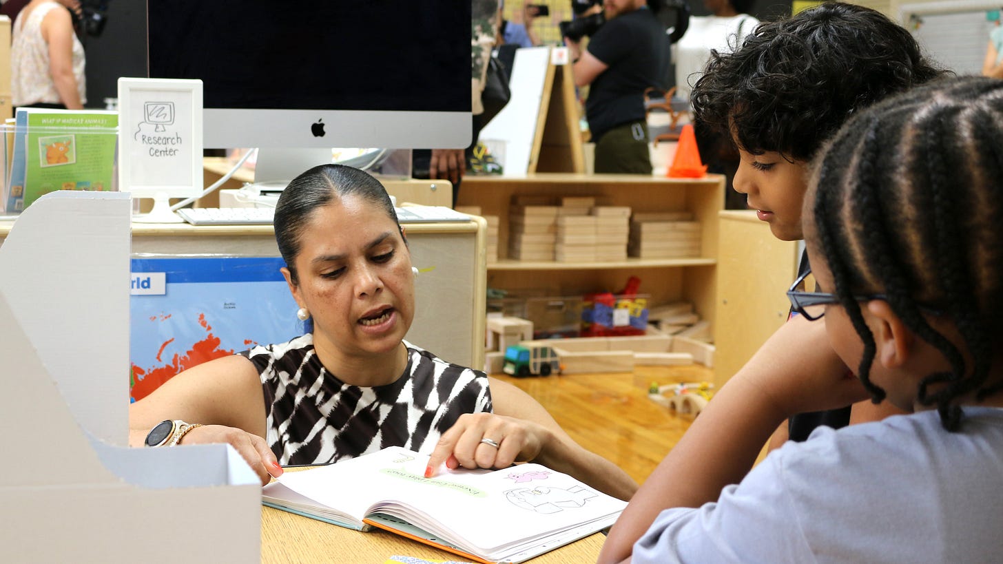 A woman points at a page in a book while two students watch